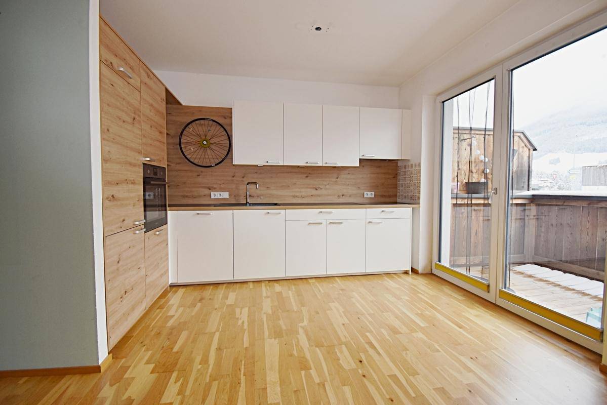 Moderne Küche mit weißen und holzfarbenen Schränken, Einbaugeräten und Balkonzugang.