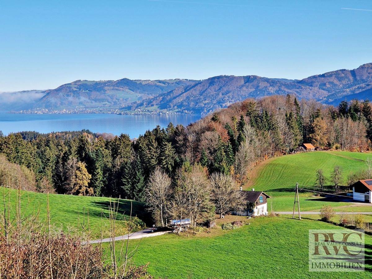 Idyllische Landschaft mit See, Bergen und vereinzelten Häusern in ländlicher Umgebung.