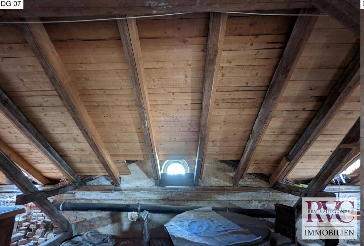 Unausgebauter Dachboden mit sichtbaren Holzbalken und einem kleinen runden Dachfenster.