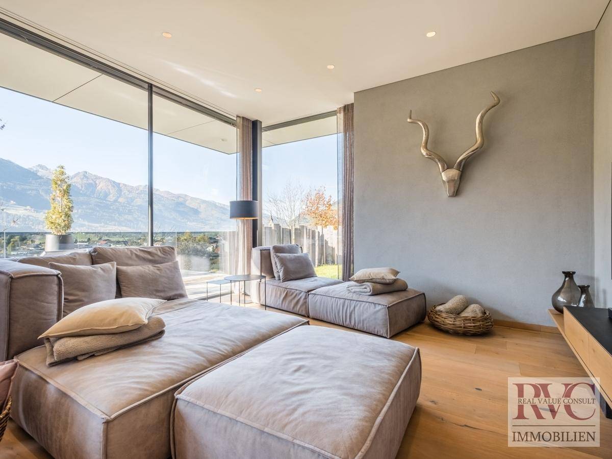 Helles Wohnzimmer mit bodentiefen Fenstern, modernen Sofas und einem atemberaubenden Bergblick.