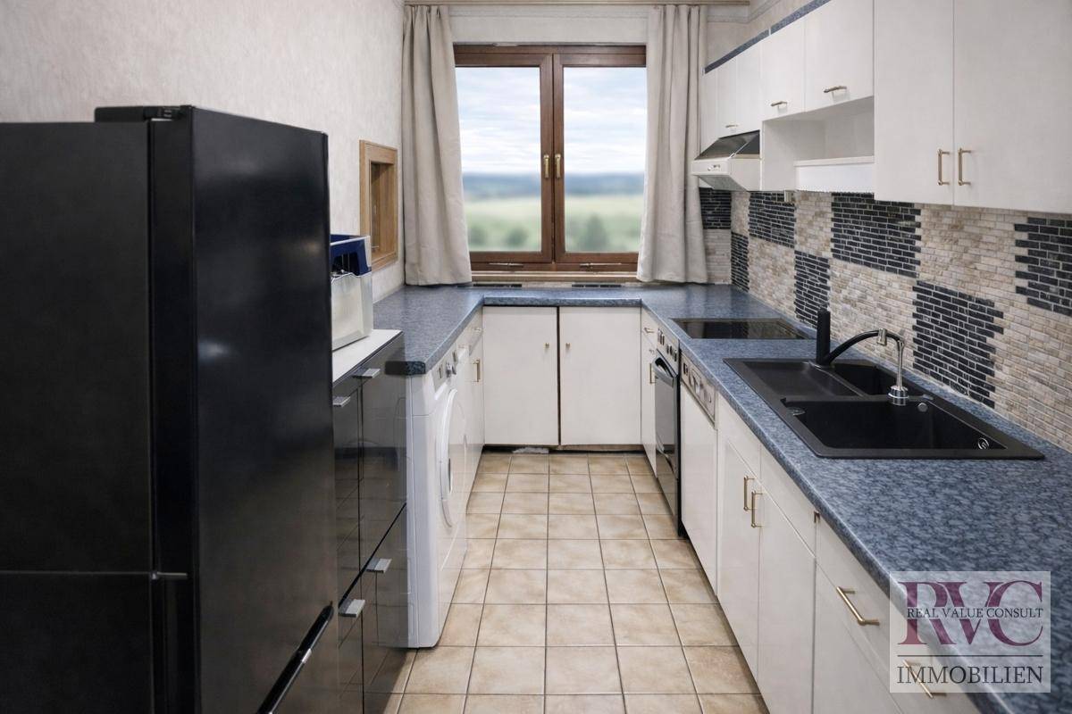 Funktionale Küche mit dunklem Kühlschrank, blauer Arbeitsplatte und Fensterblick ins Grüne.