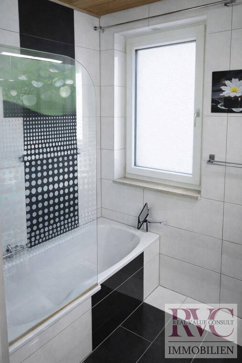 Badezimmer mit Badewanne, Duschabtrennung und schwarz-weißen Fliesen, inklusive Fenster.