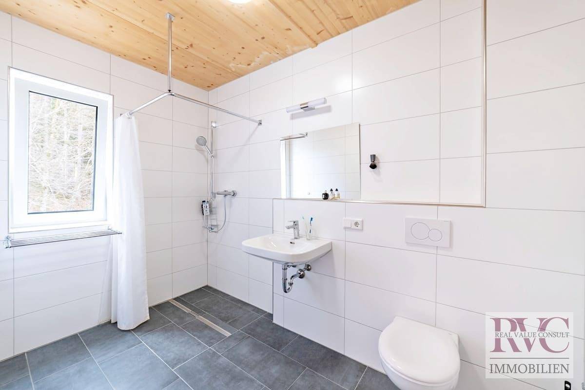Modernes Badezimmer mit weißen Wandfliesen, grauen Bodenfliesen, Dusche und Fenster.