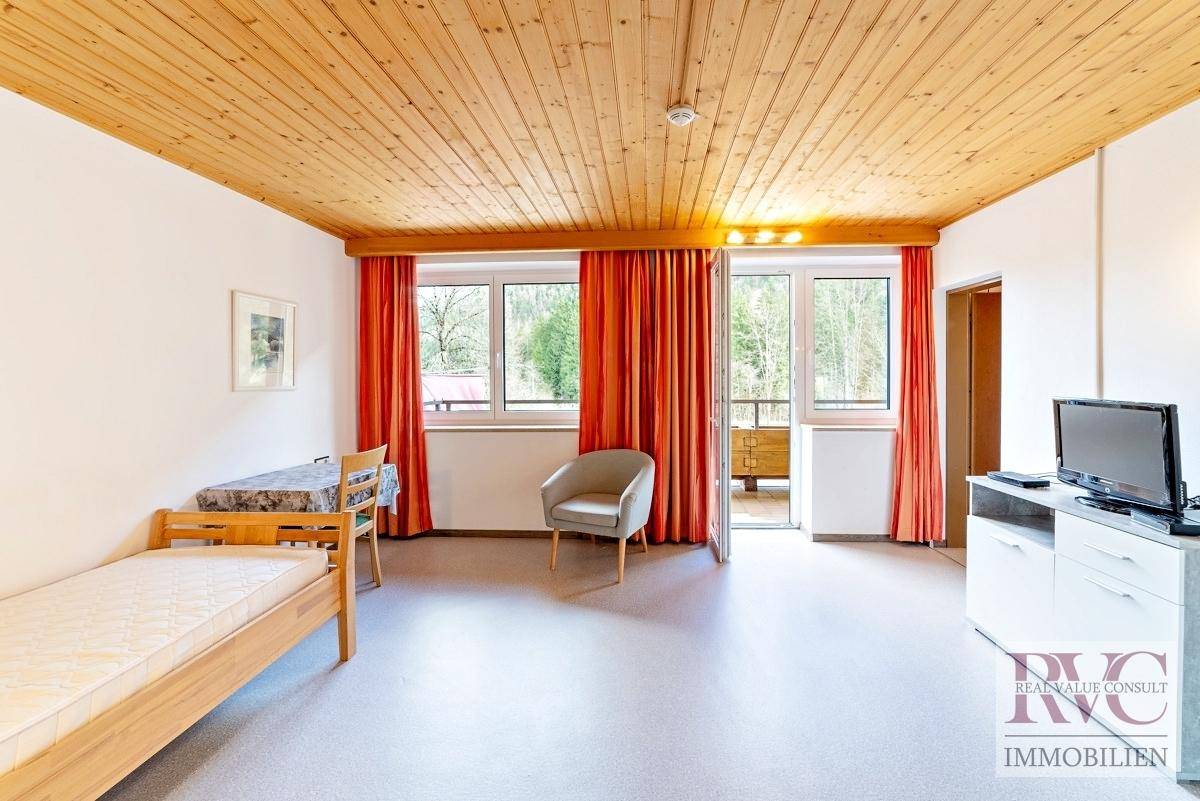 Einfaches Schlafzimmer mit Einzelbett, Holzbalkendecke und Zugang zu einem kleinen Balkon.