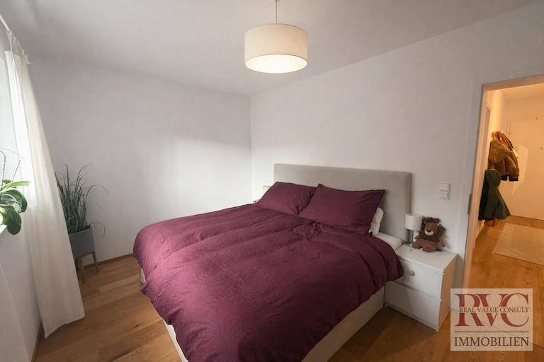 Gemütliches Schlafzimmer mit Doppelbett, Holzboden und schlichten weißen Wänden.