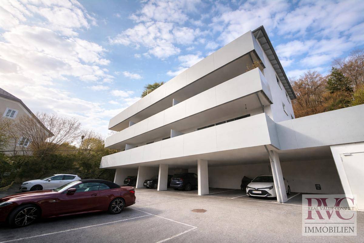 Moderne Wohnanlage mit weißer Fassade, Balkonen und überdachten Parkplätzen im Freien.