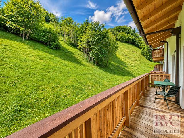 Sonniger Holz-Balkon mit Sitzgelegenheiten und weitem Blick auf grüne Hügel und Wald.