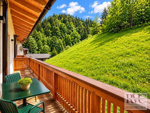 Geräumiger Holz-Balkon mit Tisch und Stühlen, umgeben von grünen Wiesen und Bäumen.