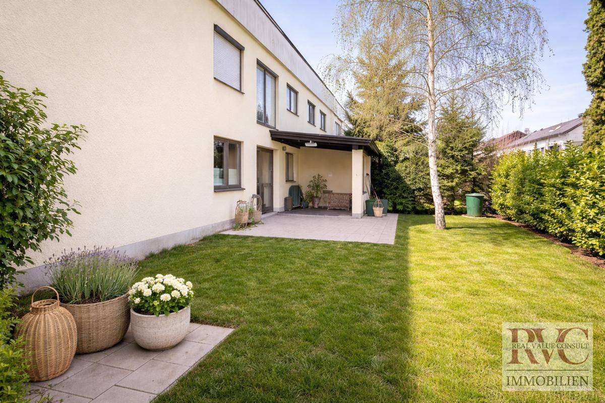 Rückseite des Hauses mit gepflegtem Rasen, Terrasse und üppiger Bepflanzung.