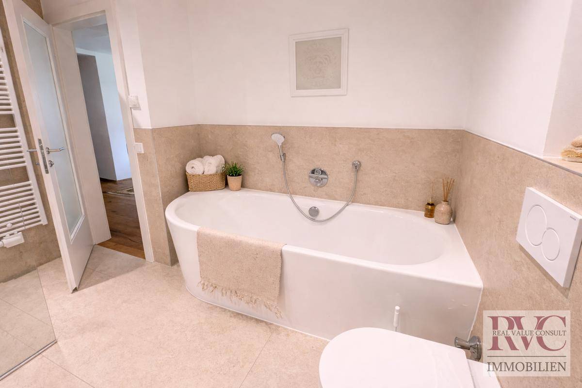 Helles Badezimmer mit Eckbadewanne, wandhängendem WC und beigen Fliesen.