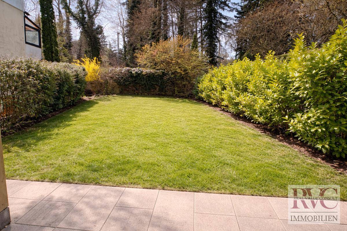 Weitläufiger Garten mit gepflegtem Rasen und vielfältiger Bepflanzung unter blauem Himmel.