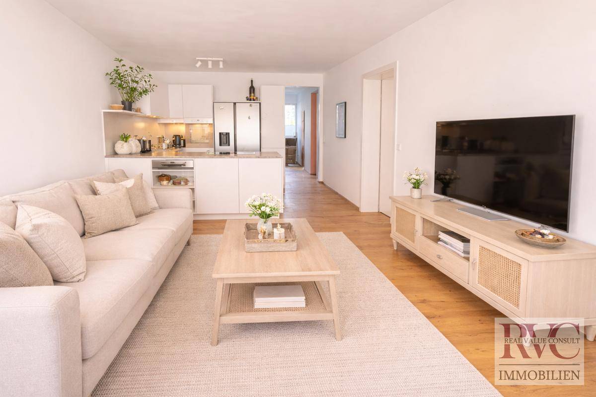 Heller Wohnbereich mit beigem Sofa, Couchtisch und offener Verbindung zur modernen Küche.