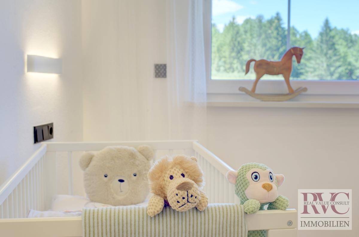 Detailansicht eines Kinderzimmers mit Babybett, Stofftieren und Blick ins Grüne.