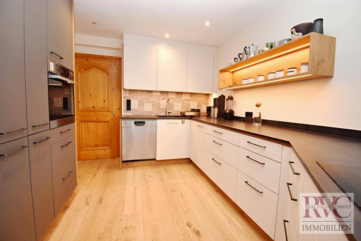 Moderne Küche mit weißen und grauen Schränken, Einbaugeräten und Holzboden.