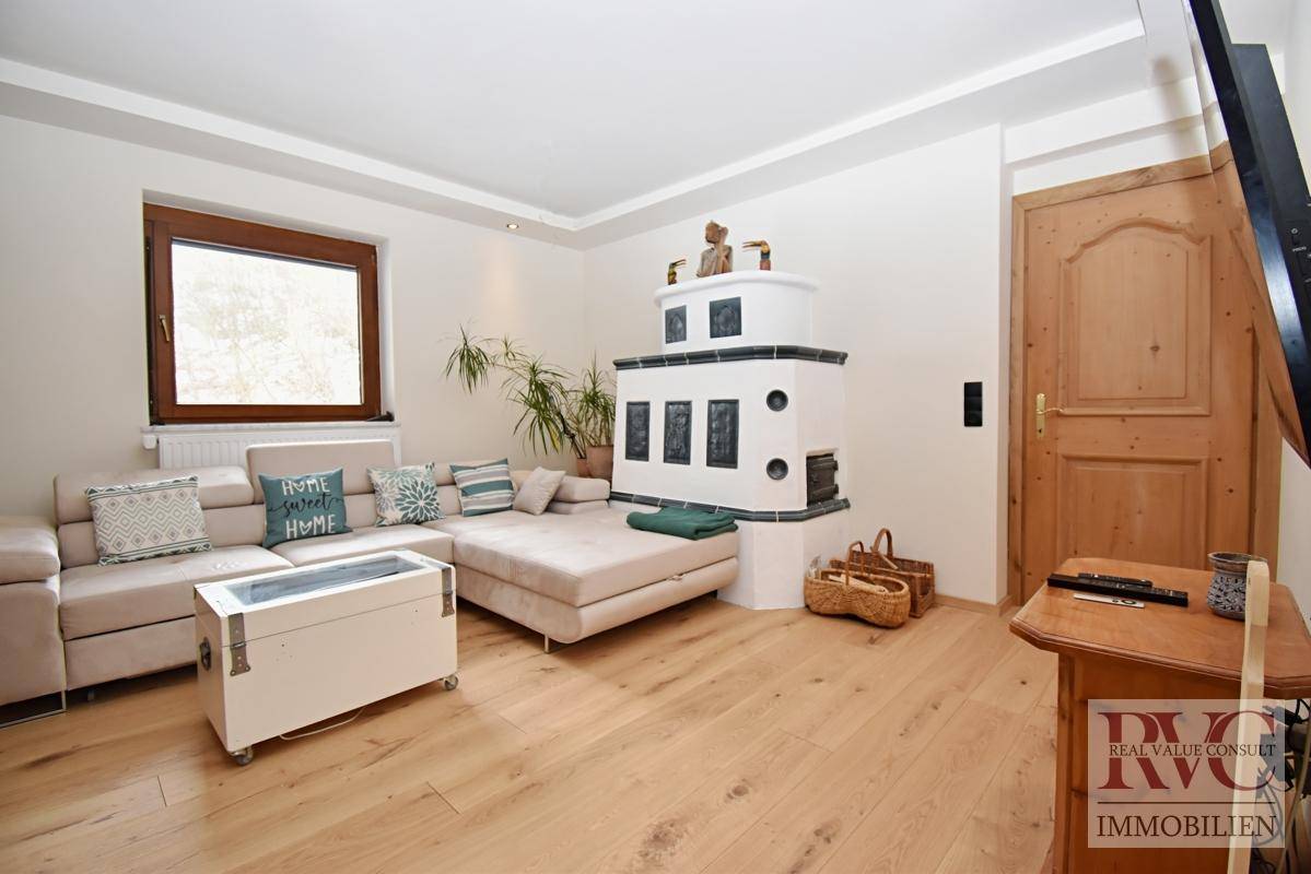 Wohnzimmer mit traditionellem Kachelofen, bequemer Couch und hellem Holzboden.