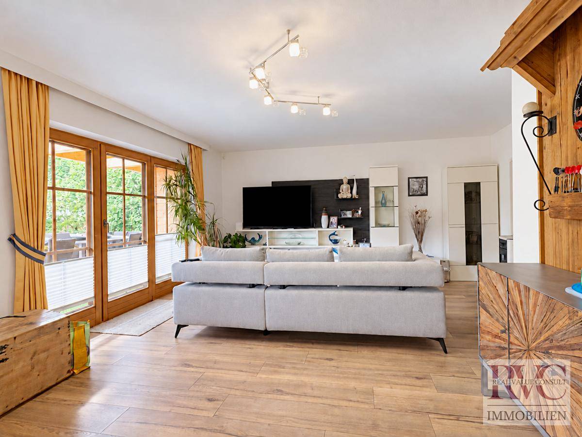 Helles Wohnzimmer mit beigem Sofa, Holzboden und Zugang zu einem Außenbereich.