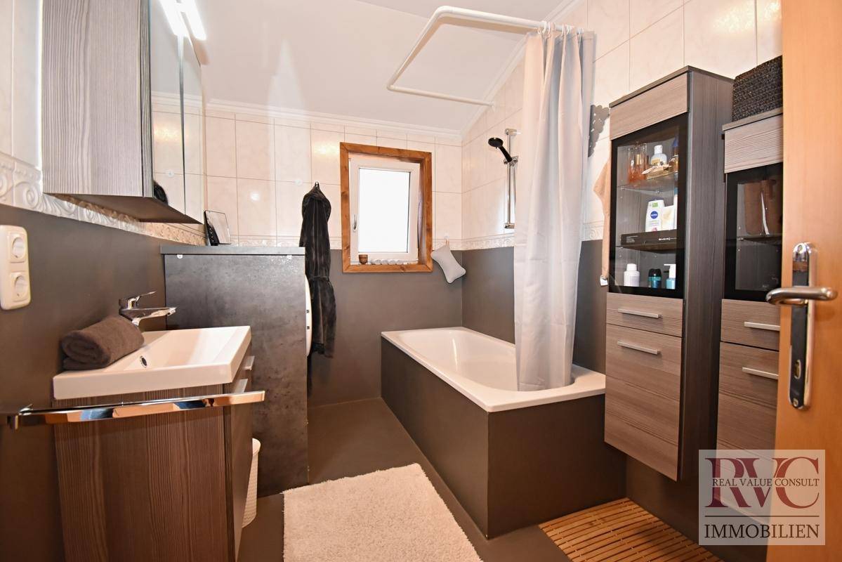 Modernes Badezimmer mit Badewanne, Fenster und dunklen Fliesen im unteren Bereich.