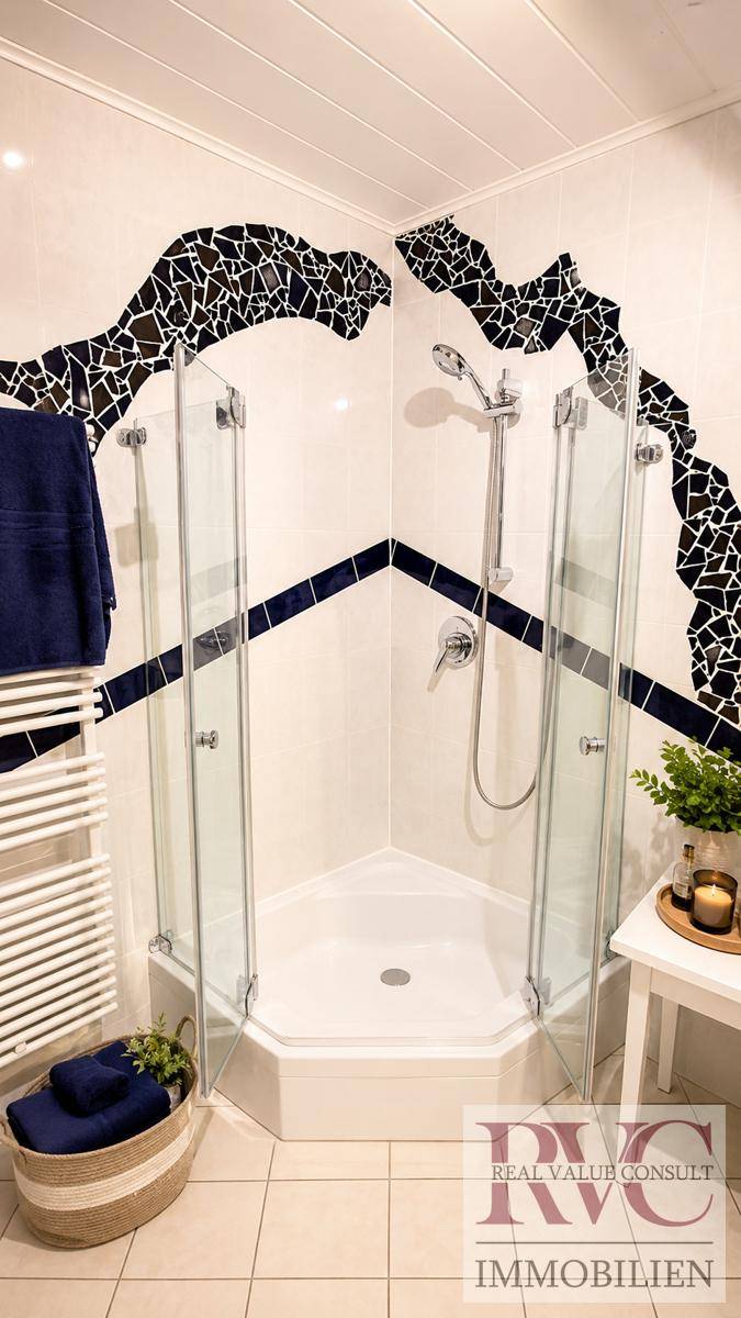 Badezimmer mit Eckdusche, weißen Fliesen und dekorativen schwarzen Mosaikakzenten an der Wand.