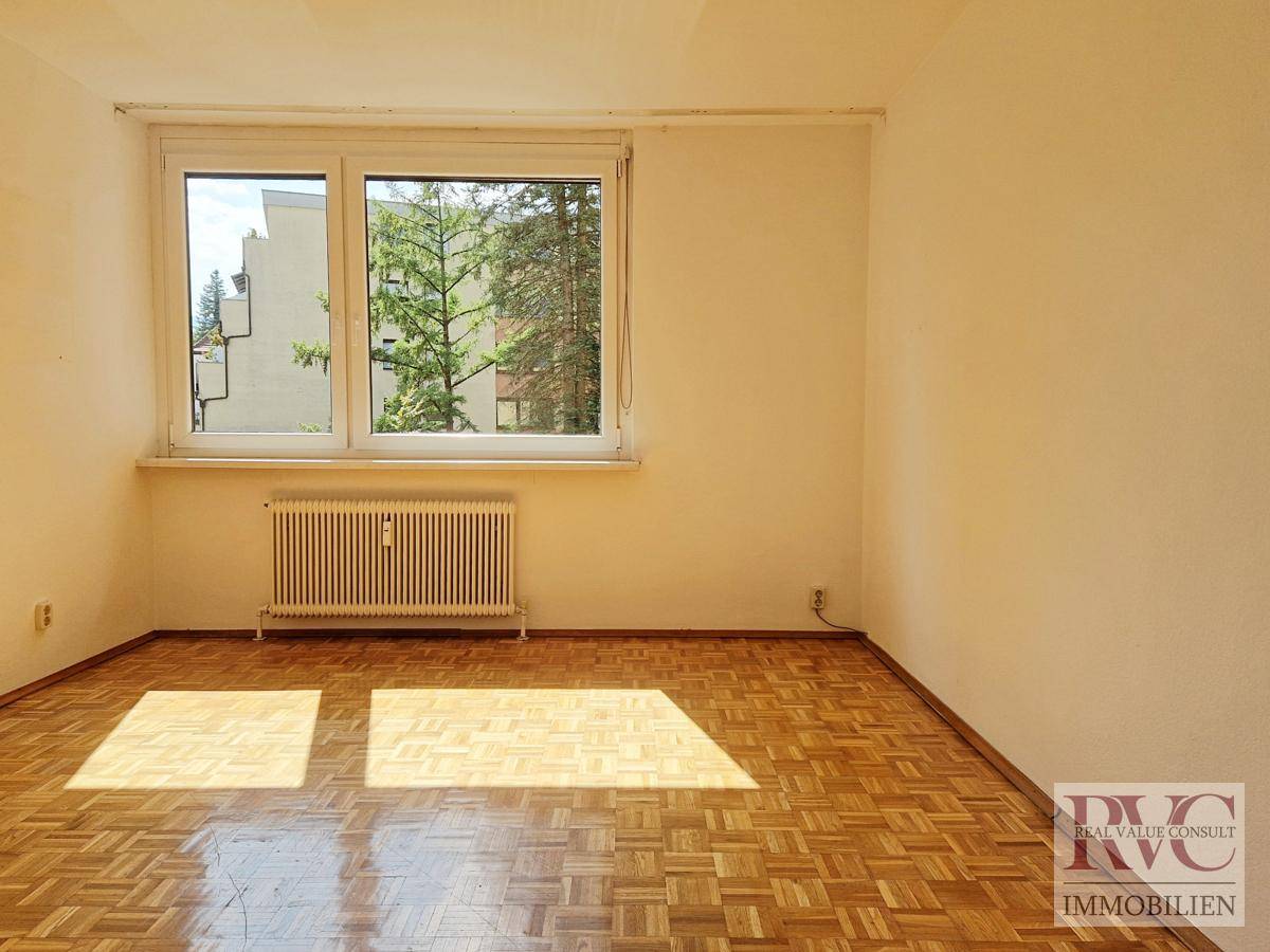 Helles Schlafzimmer mit Parkettboden und Blick ins Grüne.