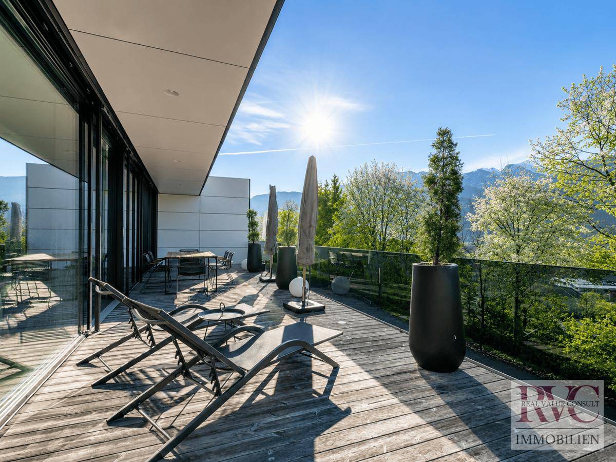 Sonnige Holzterrasse mit Liegestühlen, Sonnenschirmen und Panoramablick auf die umliegende Landschaft.