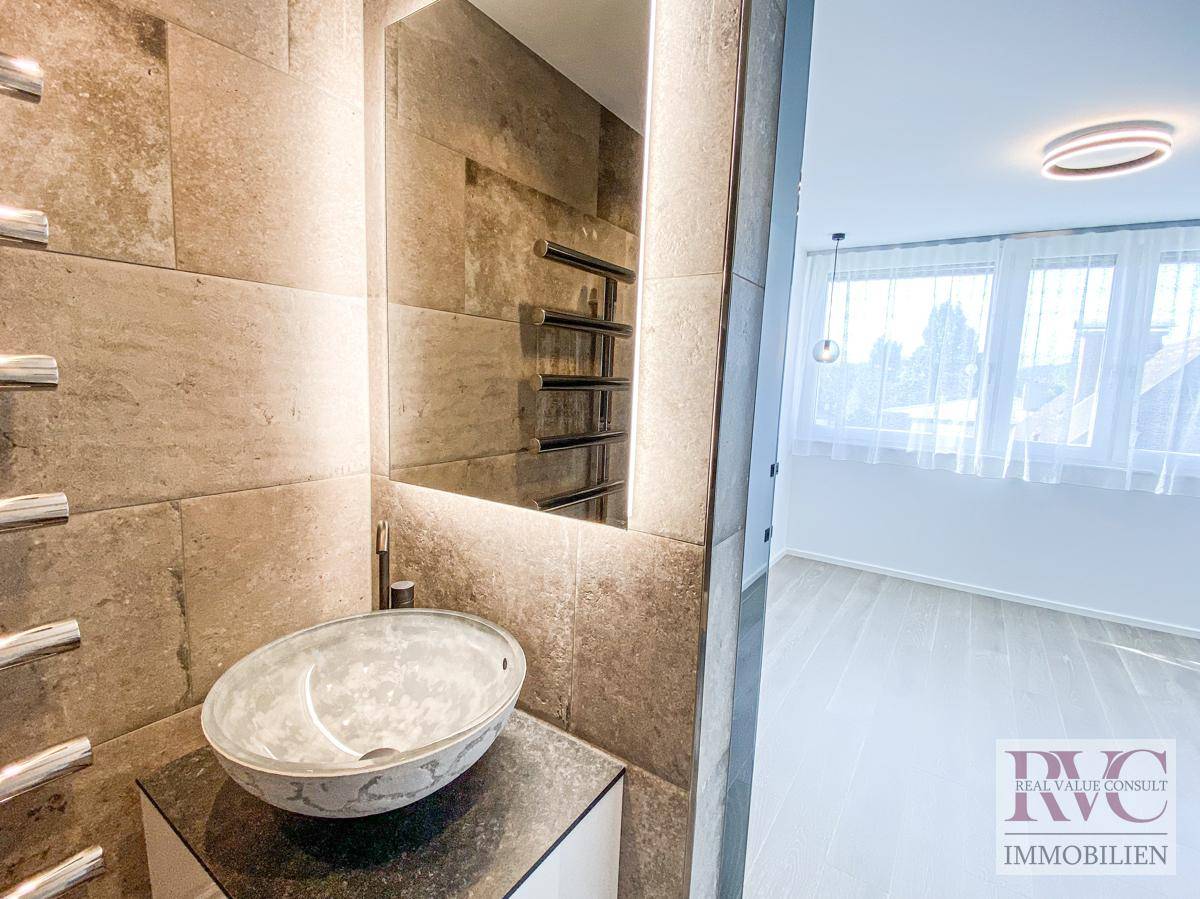 Elegantes Badezimmer mit modernem Aufsatzwaschbecken, beleuchtetem Spiegel und Fliesenwänden.