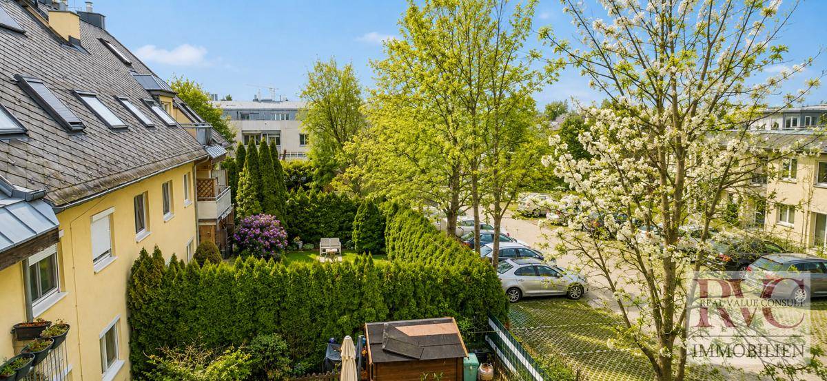 Rückansicht des Wohngebäudes mit Gartenbereich, Hecken und einem Parkplatz im Hintergrund.