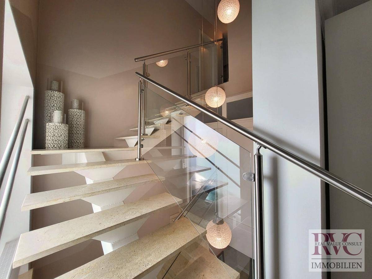 Moderne Treppe mit Glasgeländer, Steinstufen und stilvoller Beleuchtung.