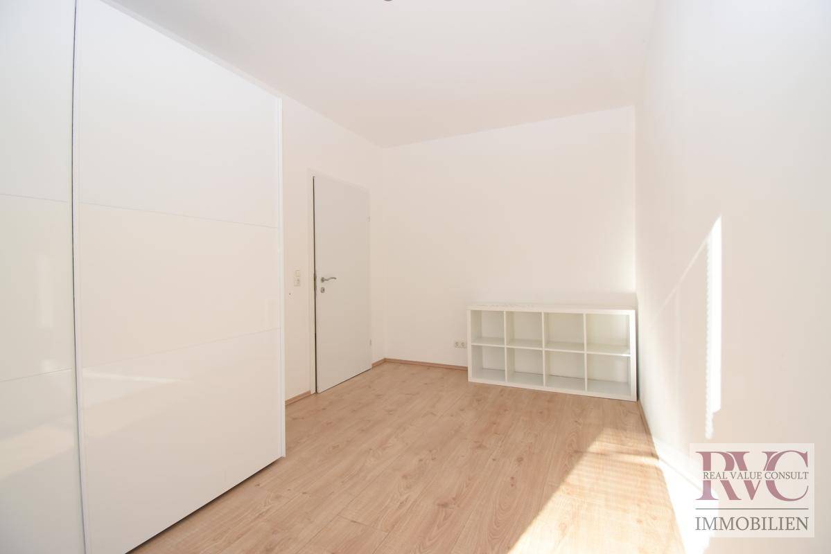 Helles Zimmer mit weißem Kleiderschrank, Regal und Laminatboden.