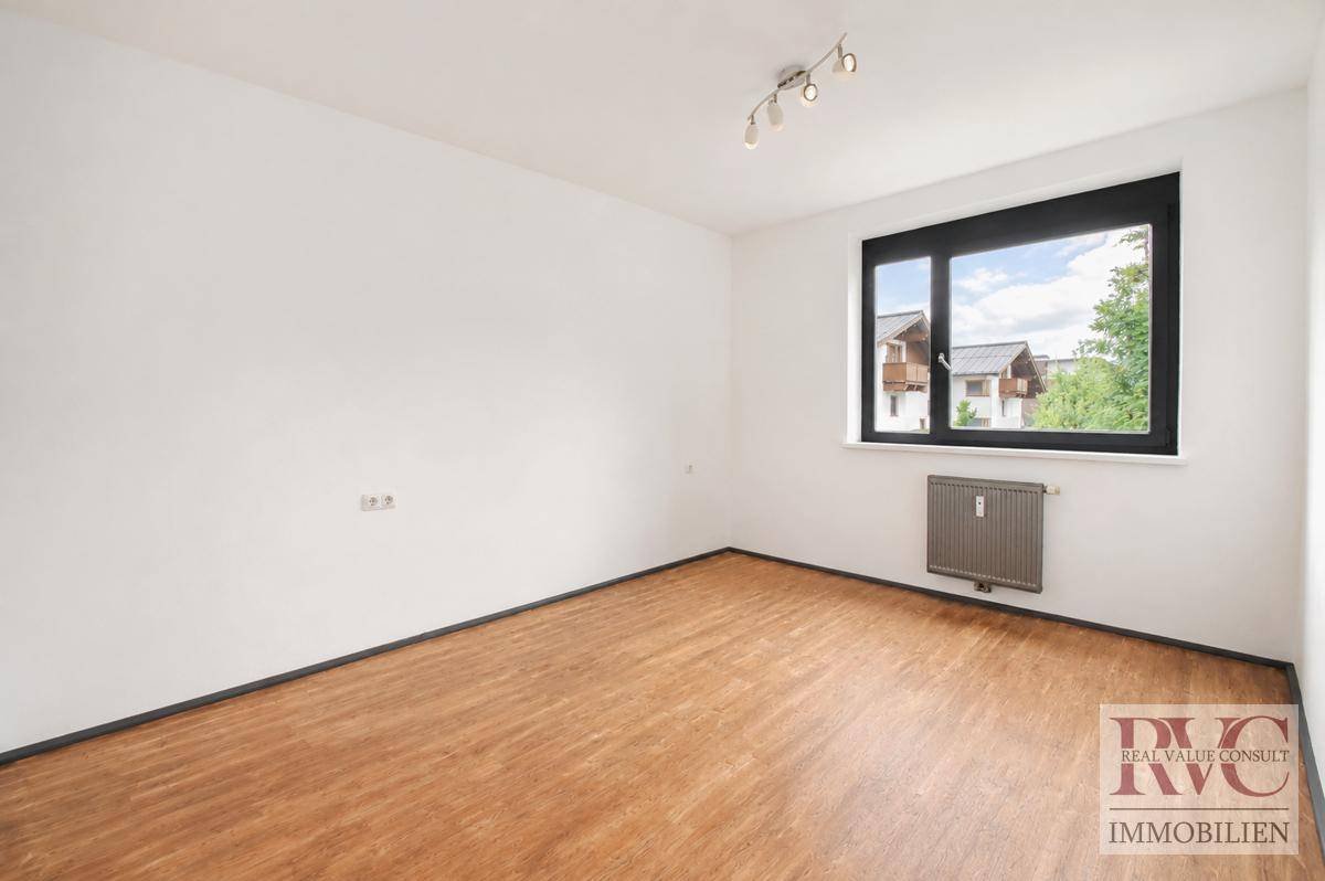 Leeres Zimmer mit Holzboden, großem Fenster und Heizkörper.