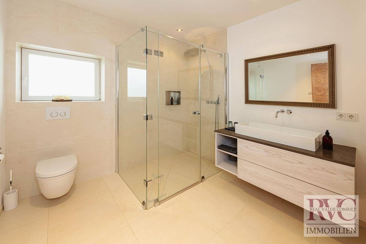 Modernes Badezimmer mit großer Glasdusche, Waschtisch und Fenster.