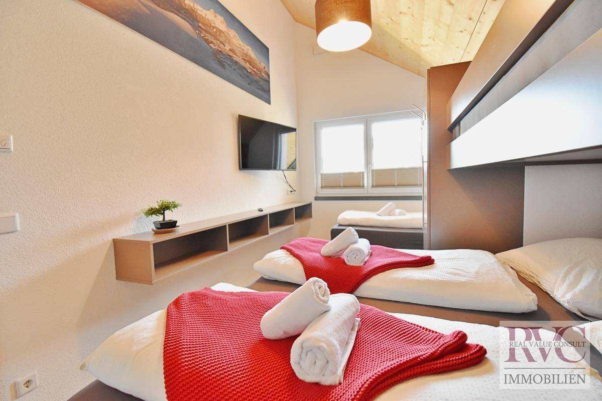Helles Schlafzimmer mit Etagenbett, Einzelbetten, Holzdachschräge und Fernseher an der Wand.
