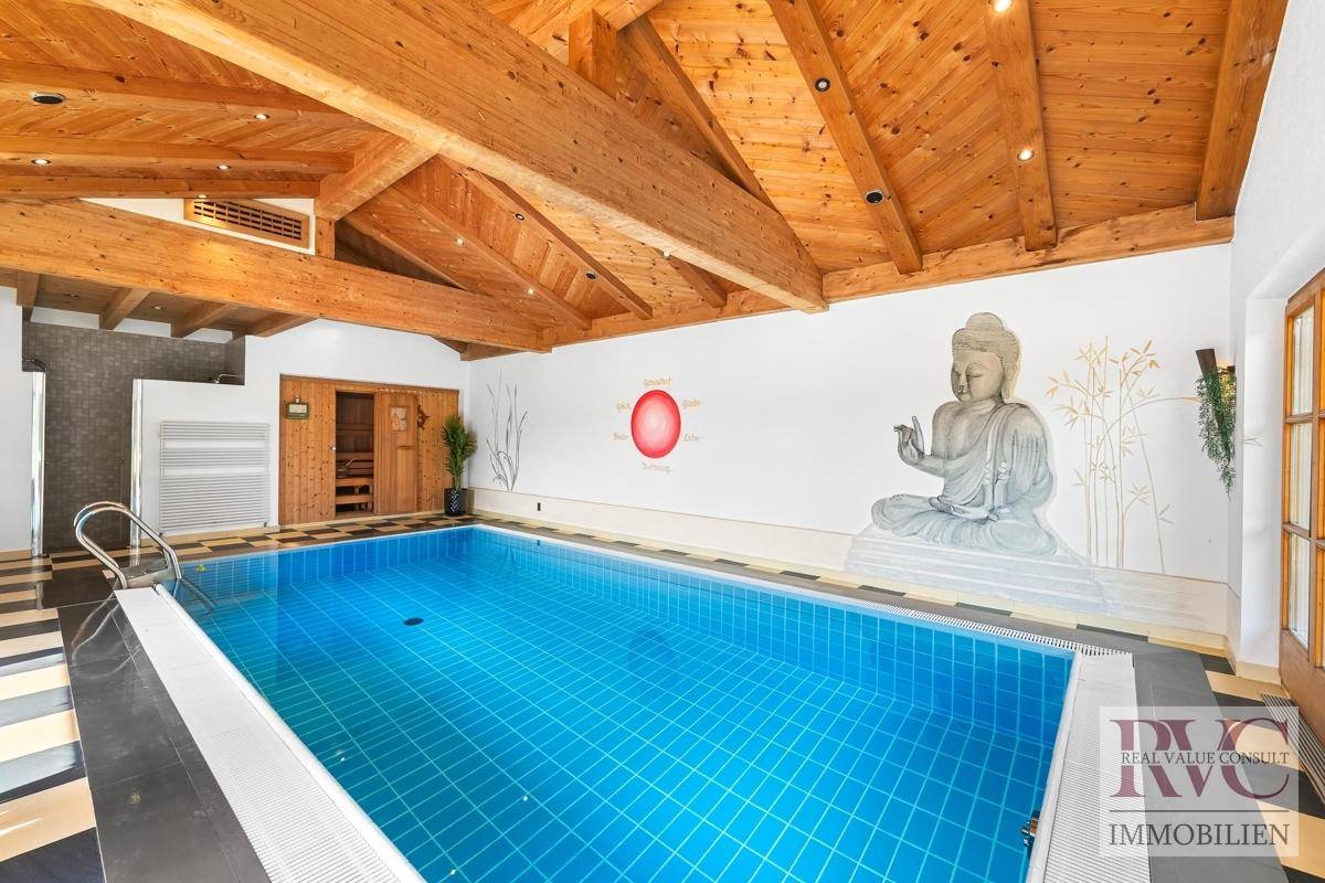 Geräumiger Innenpool mit Holzbalkendecke, Zugang zur Sauna und Blick ins Grüne durch große Fenster.