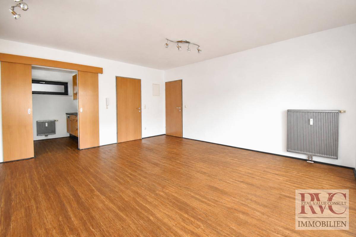Heller Wohnbereich mit Holzboden, Heizkörper und Zugang zu weiteren Räumen.