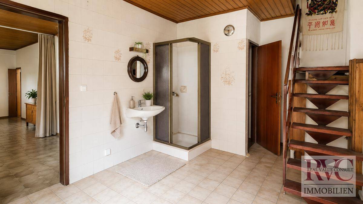 Funktionales Badezimmer mit Duschkabine, Waschbecken und Holzdecke, daneben eine Holztreppe.