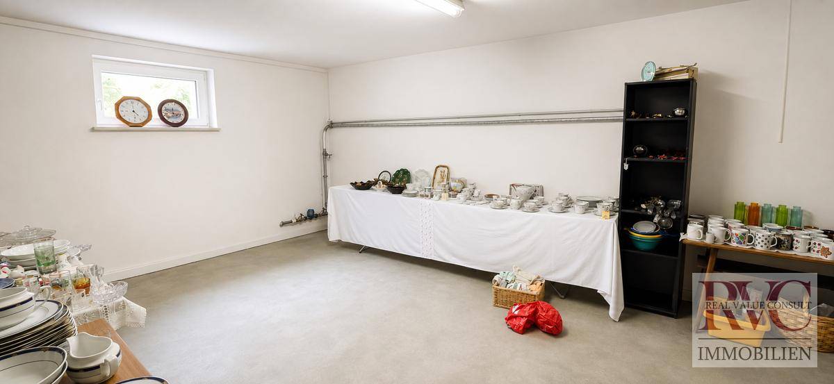 Geräumiger Abstellraum mit Fenster, Betonboden und Regalen voller Geschirr.