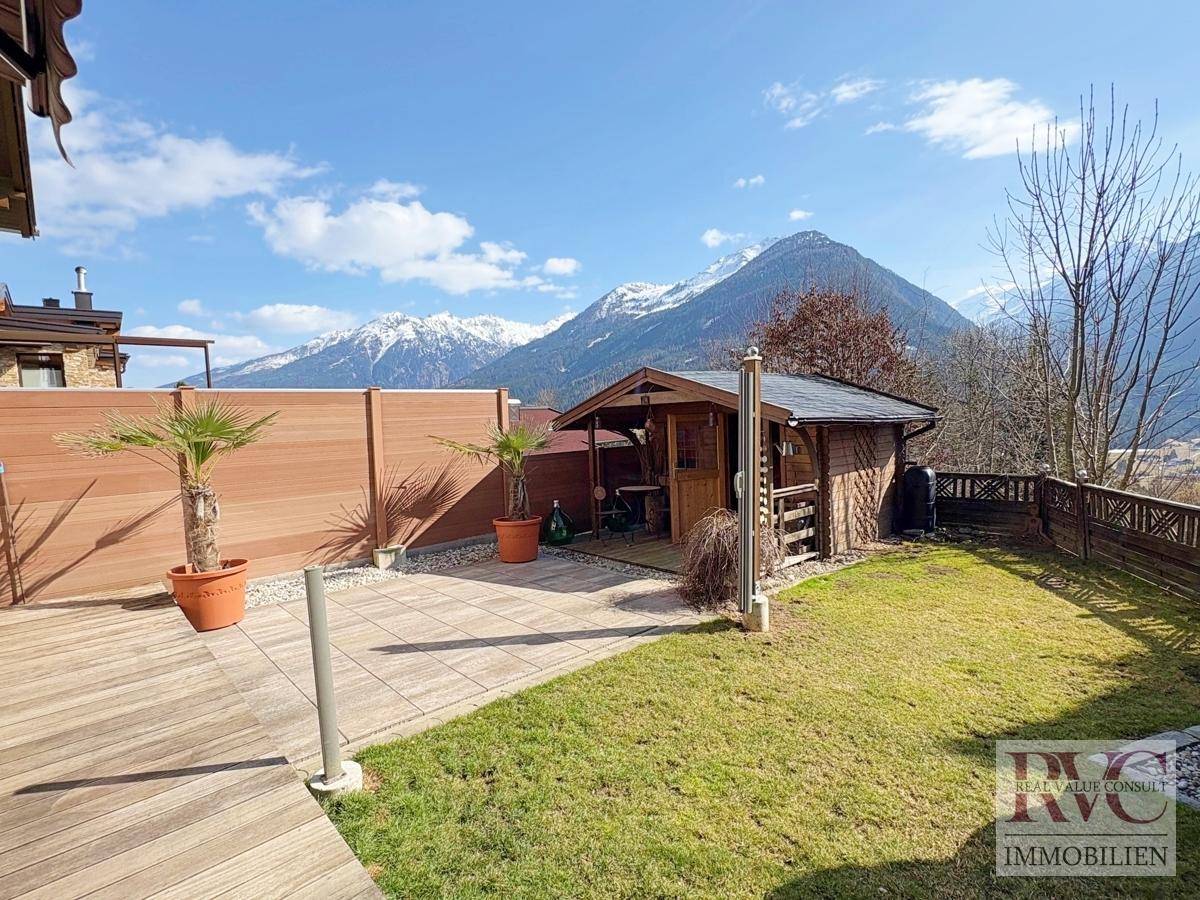 Gepflegter Garten mit Rasenfläche, Holzschuppen und Panoramablick auf die Berge.