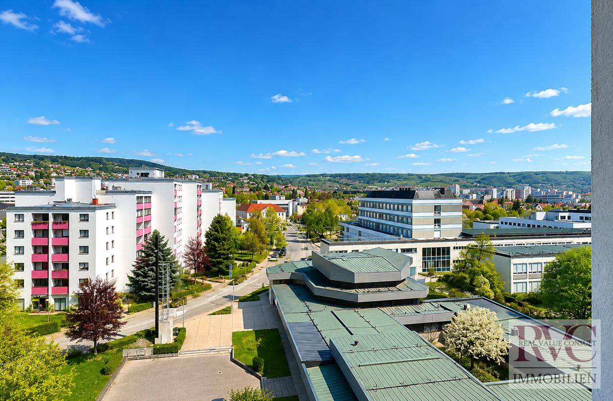 Weitläufiger Blick über ein Wohngebiet mit mehreren Gebäuden und Grünflächen unter blauem Himmel.