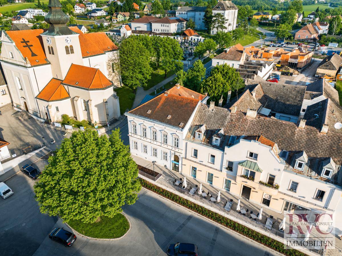 Panoramablick auf eine historische Stadt mit einer Kirche, traditionellen Gebäuden und grüner Umgebung.