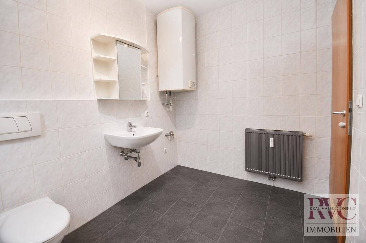 Helles Badezimmer mit Waschbecken, WC, Boiler und Heizkörper.