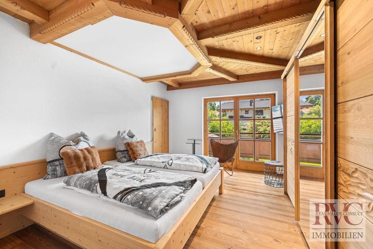 Gemütliches Schlafzimmer mit Holzbett, Holzbalkendecke und Zugang zu einem sonnigen Balkon.