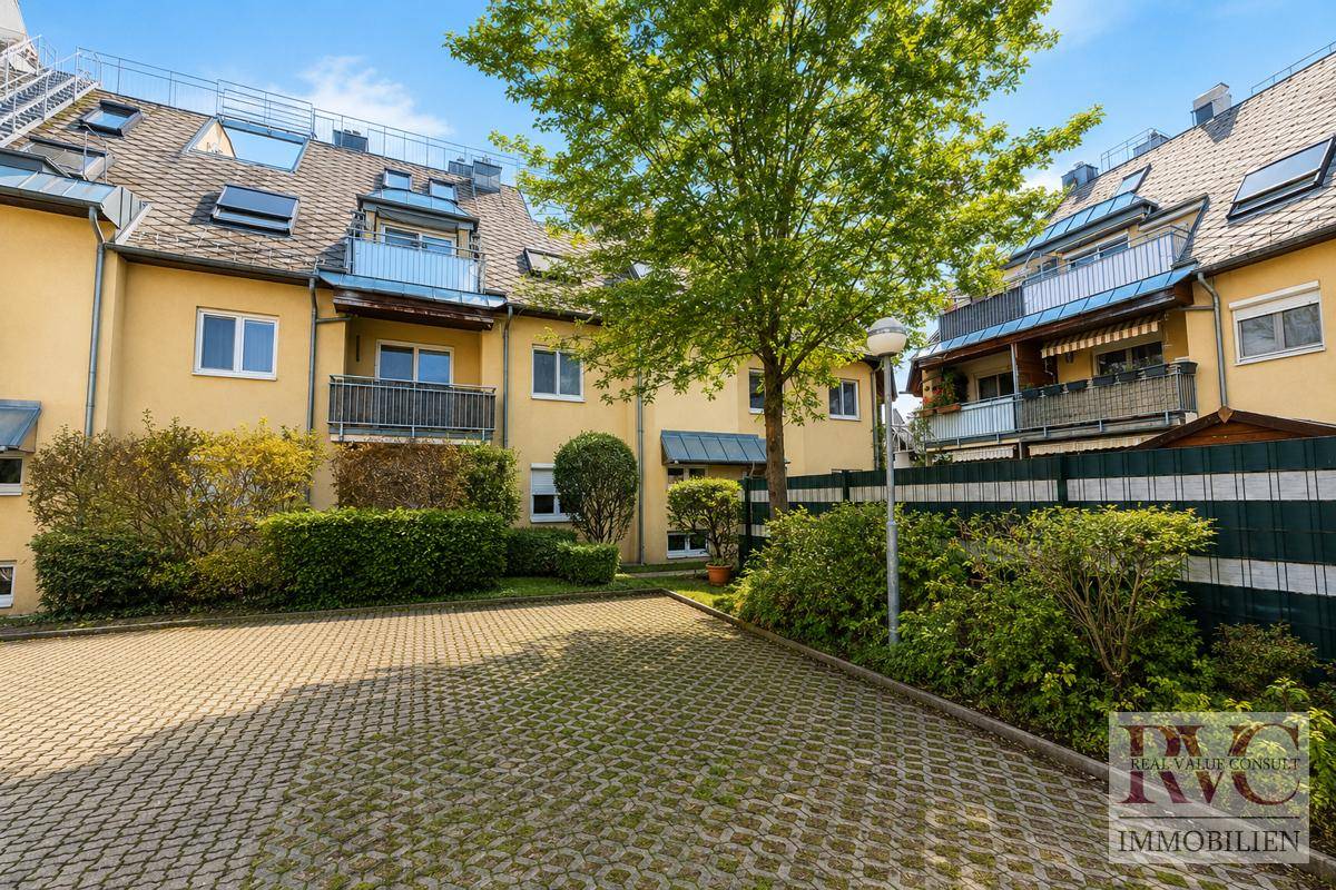 Außenansicht eines Wohnkomplexes mit gelben Fassaden, Balkonen und einem gepflasterten Parkplatzbereich.
