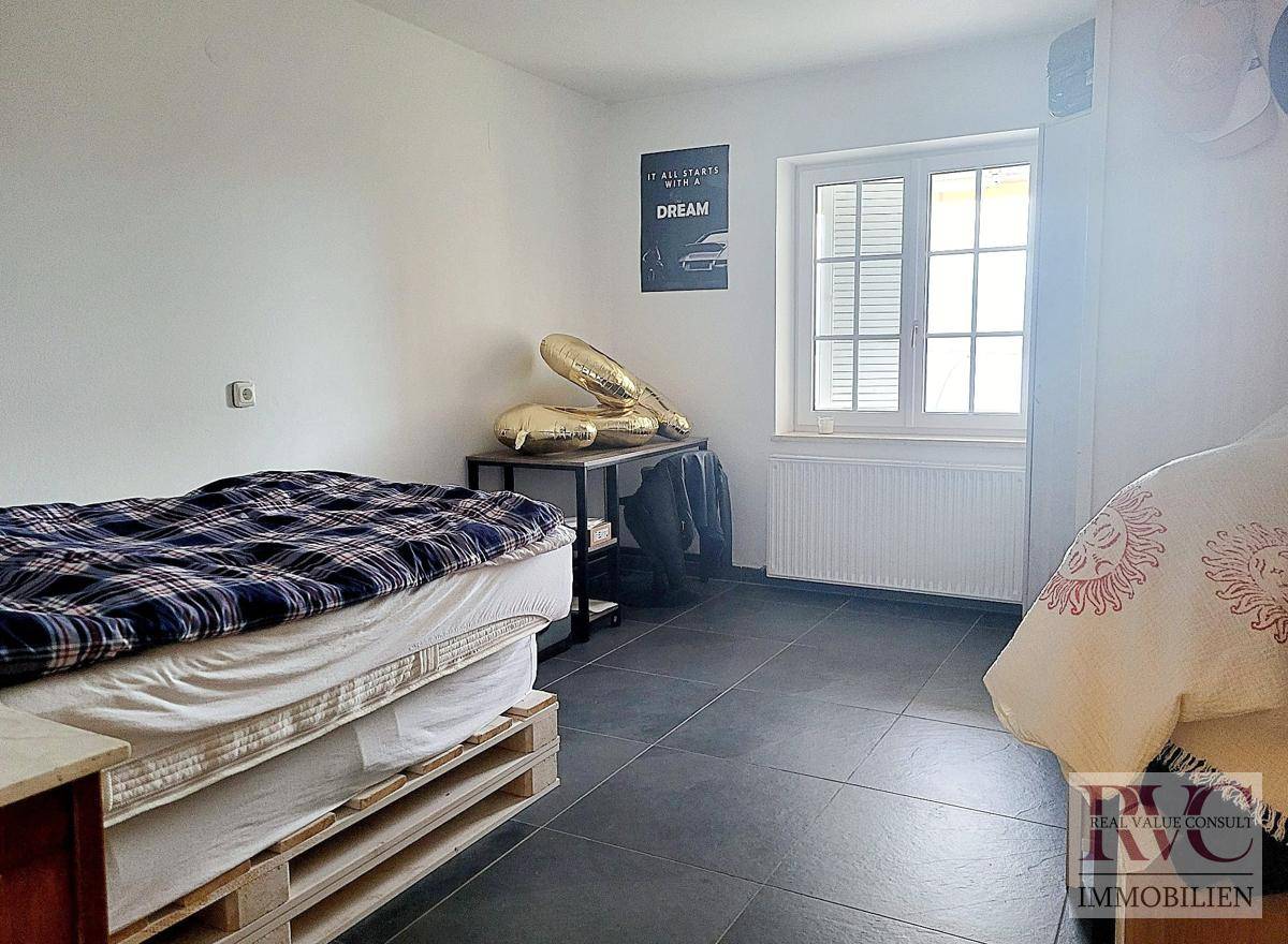Schlafzimmer mit zwei Betten, dunklem Fliesenboden und einem Fenster für Tageslicht.