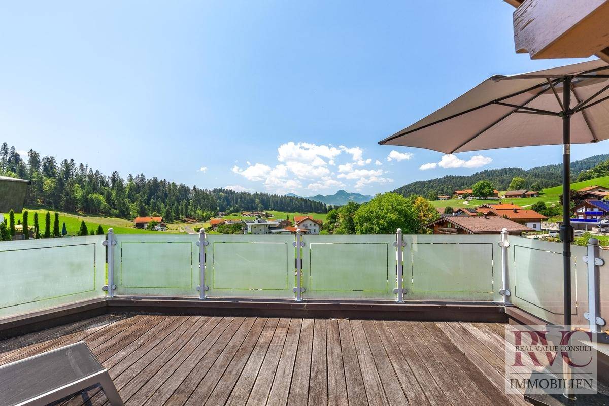 Sonnige Holzterrasse mit moderner Glasbrüstung und weitem Blick über die grüne Hügellandschaft.
