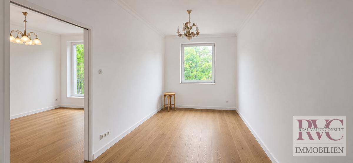 Helles, leeres Zimmer mit Holzboden und großen Fenstern, ideal für ein Schlaf- oder Wohnzimmer.