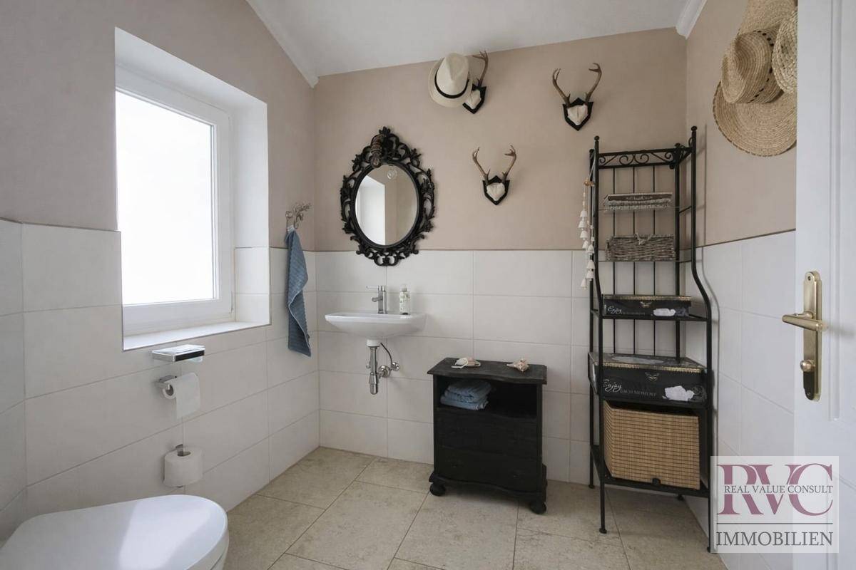 Badezimmer mit Fenster, WC, Waschbecken und rustikalen Hirschgeweih-Dekorationen an der Wand.