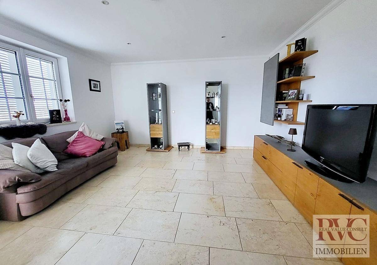 Gemütliches Wohnzimmer mit Sofa, TV-Möbeln, Regalen und hellen Fliesen auf dem Boden.