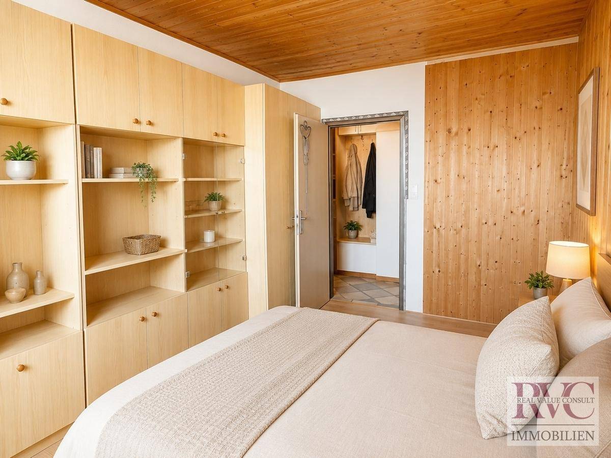Schlafzimmer mit hellen Holzschränken, Holzbalkendecke und Zugang zu einem begehbaren Kleiderschrank.