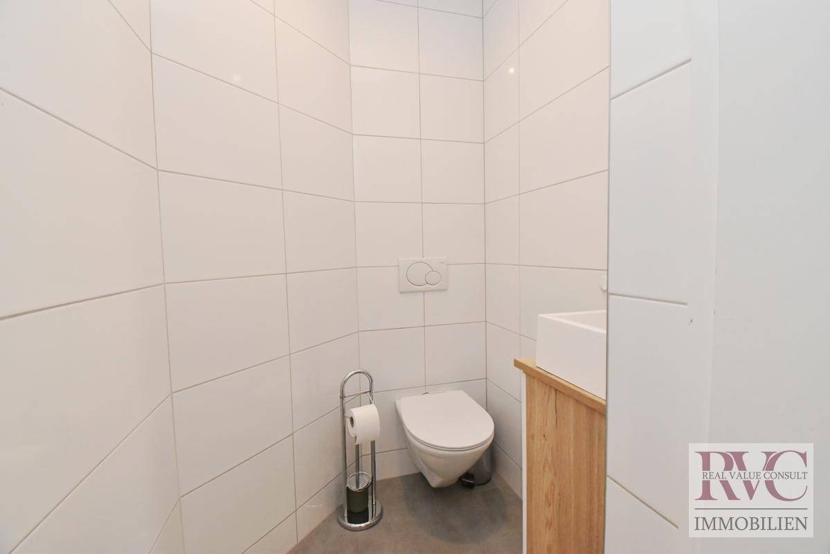 Gäste-WC mit wandhängender Toilette und kleinem Waschbecken in schlichtem, modernem Design.