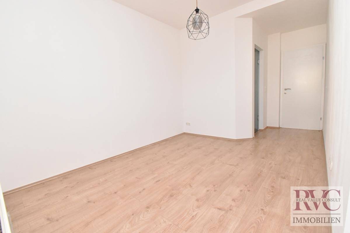 Leerer Raum mit hellem Laminatboden und weißen Wänden, bereit zur individuellen Gestaltung.