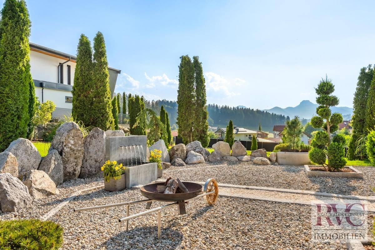 Mediterraner Gartenbereich mit Kiesflächen, großen Steinen, Feuerstelle und hohen Zypressen.